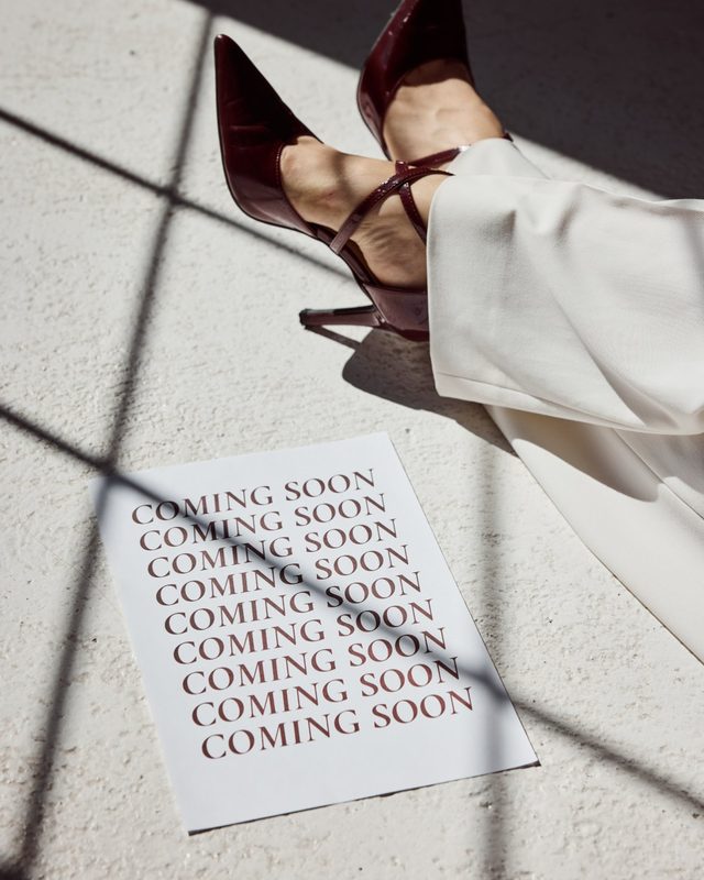 Blatt mit „Coming soon“ neben bordeauxroten Schuhen im Sonnenlicht